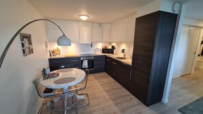 Una cocina moderna con una isla de mármol, taburetes de bar, horno empotrado y una pared acentuada en madera oscura.