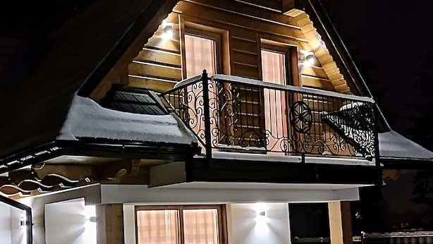 Ett modernt hus i två våningar med en balkong, stora fönster och en väl upplyst fasad.