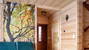 En stuga med träpanel på insidan, en turkosfärgad soffa, en trätrappa och en dörr som leder till ett annat rum.