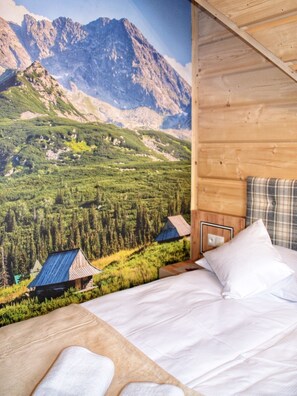 Ein Schlafzimmer mit Bett, Kissen und Blick auf eine Berglandschaft mit einer Hütte.