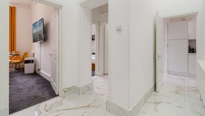 Ein Hotelgang mit Essbereich, einem an der Wand befestigten Fernseher und einem durch eine offene Tür einsehbaren Badezimmer.