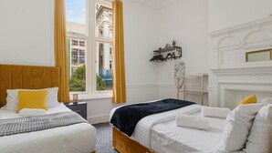 Ein Hotelzimmer mit zwei Betten, einem Fenster mit Vorhängen, einem kleinen Tisch und einem Kamin.