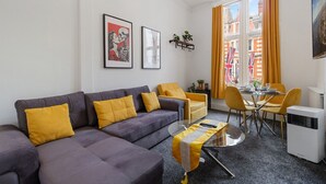 Ein modernes Wohnzimmer mit einem grauen Sofa, gelben Kissen, einem Glastisch und einem Essbereich mit gelben Stühlen und einem Tisch.
