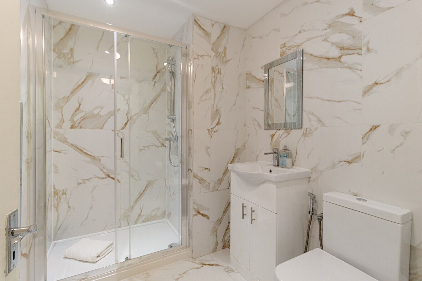 A bathroom with a glass-enclosed shower, a white sink, and a toilet.