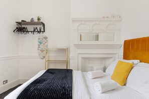 A hotel room with a bed, a wooden headboard, a fireplace, a shelf with towels, and a geometric wall decoration. - Flat 6 Oxford · Apartment Oxford Street Bond Street Station. (Greater London)