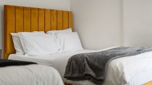 Uma cama com cabeceira de madeira, roupa de cama branca e manta cinza.
