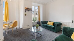 A modern living room with a green sofa, yellow cushions, a glass coffee table, and a dining area with yellow chairs. - Luxury at Your Doorstep: 2-Bedroom Gem on Oxford Street -10 (Greater London)
