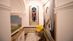 A hallway with a marble floor, a yellow chair, a statue, a painting, and a framed portrait.