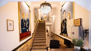 A reception area with a staircase, a chandelier, and framed portraits on the walls.