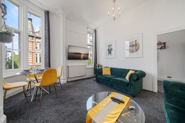 A modern living room with a green sofa, yellow chairs, a glass coffee table, and a TV mounted on the wall. - Oxford Street Apartments 3, Charming Three Bedroom (London)