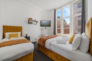 A hotel room with two beds, a TV, a fireplace, and a large window with a city view. - Oxford Street Apartments 3, Charming Three Bedroom (London)