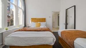 A hotel room with a large window, a bed with a wooden headboard, a bedside table, and a door.