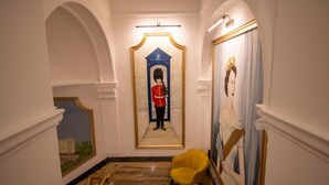 A hallway with a red double door, a yellow chair, and a large painting of a woman.