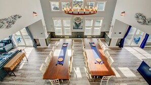Un comedor amplio con dos mesas de madera largas, sillas blancas y un candelabro central.