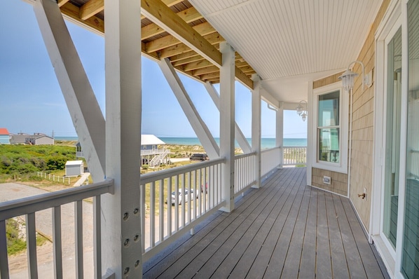 Une terrasse en bois couverte offrant une vue sur l’océan et les maisons de plage.