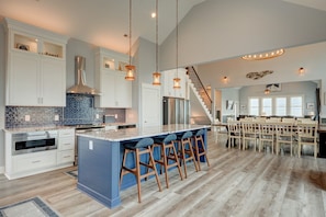 Une cuisine spacieuse dotée d’un grand îlot central, de meubles blancs et d’un dosseret en carreaux disposés en motif chevron.