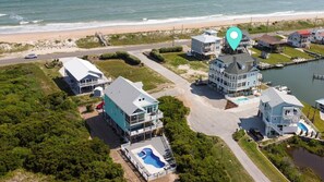 Vue aérienne d’un quartier résidentiel situé sur la côte, avec de nombreuses maisons, une piscine et une plage en arrière-plan.