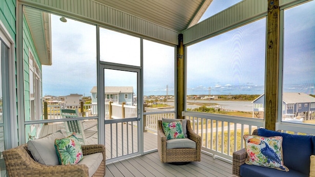 A covered porch with wicker furniture and a view of the beach and buildings. - Spacious 8-bedroom oceanview house in North Topsail Beach, perfect for gatherings! (North Topsail Beach)