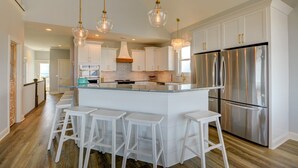 A modern kitchen with a central island, stainless steel appliances, and white cabinetry. - Spacious 8-bedroom oceanview house in North Topsail Beach, perfect for gatherings! (North Topsail Beach)