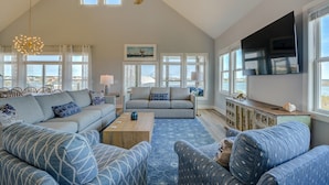 A spacious living room with a high ceiling, large windows, and a ceiling fan. - Spacious 8-bedroom oceanview house in North Topsail Beach, perfect for gatherings! (North Topsail Beach)