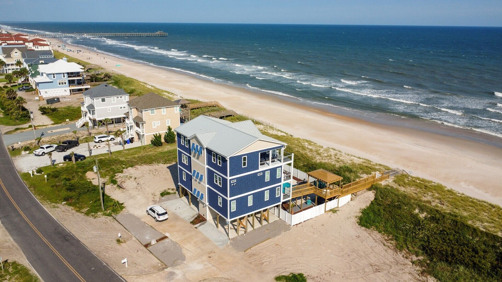 Una propiedad costera con un edificio de varios pisos, vista a la playa y un muelle al fondo.