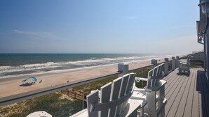 Uitzicht op het strand vanaf een balkon, met stoelen en een balustrade.