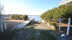 A wooden dock leading to a calm body of water, surrounded by greenery and a clear sky. - Ocean Sounds: Spacious 7BR oceanview beach house in North Topsail with ocean views! (North Topsail Beach)