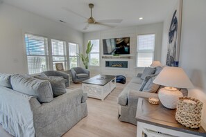 A modern living room with a flat-screen TV, a ceiling fan, and a fireplace.