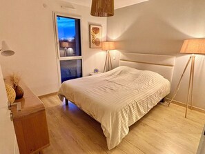 A bedroom with a bed, bedside lamp, window, and a wall-mounted picture.