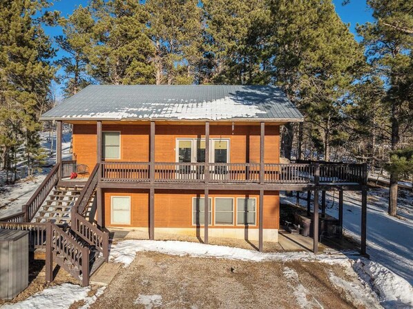 A two-story wooden cabin with a balcony, surrounded by trees and snow.