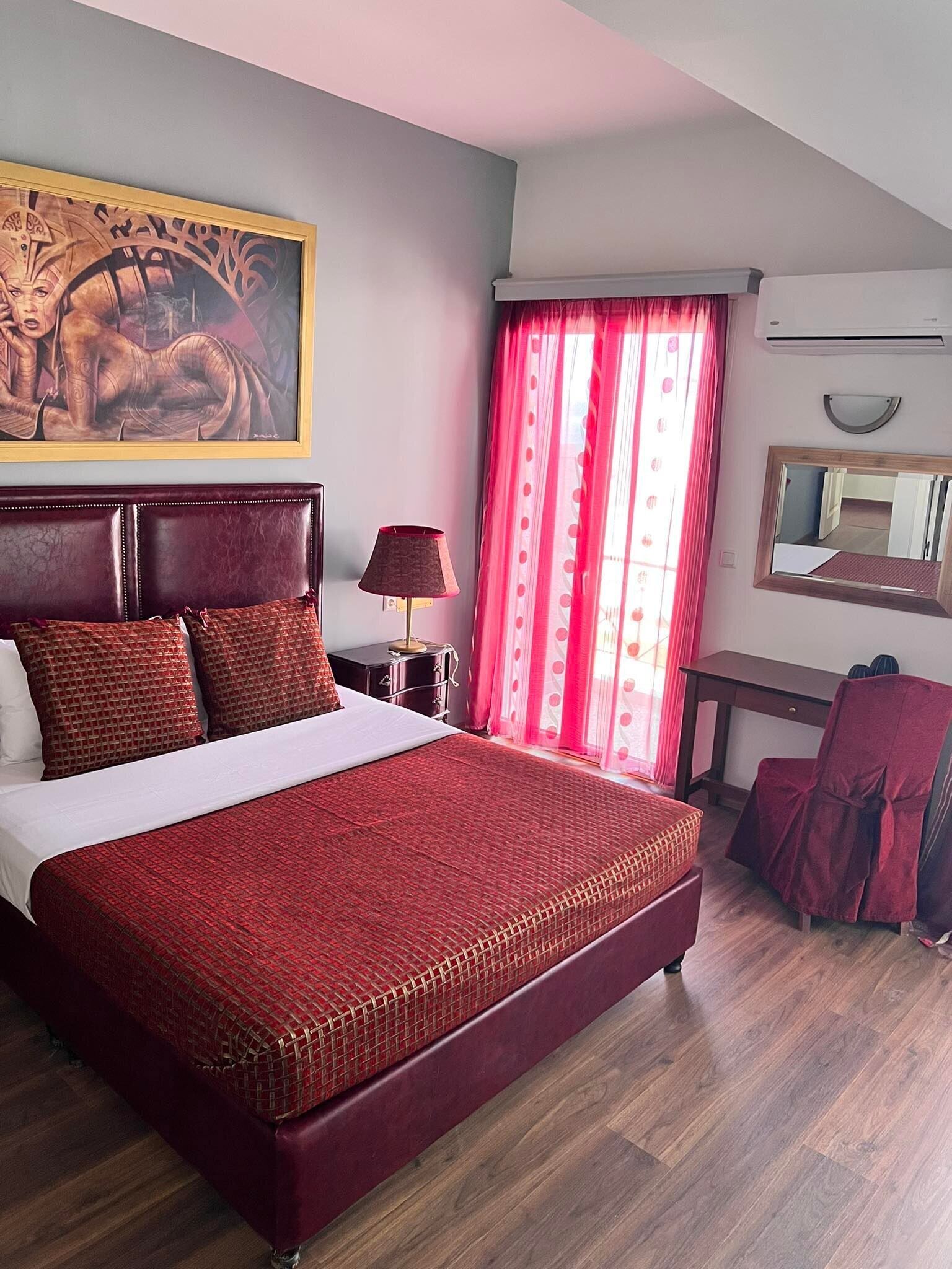 A hotel room with a large bed, a desk, a chair, a mirror, and a painting on the wall.