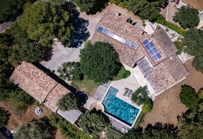 Luchtbeeld van een woonhuis met zwembad, zonnepanelen en een grote boom.