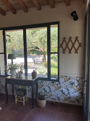 A room with a large window, a table with a lamp, a chair, and a wall-mounted decoration.