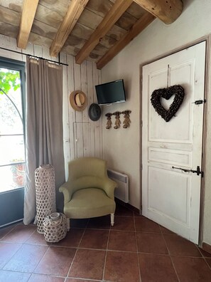 A room with a wooden ceiling, a television mounted on the wall, a heart-shaped decoration, a chair, and a door with a handle.