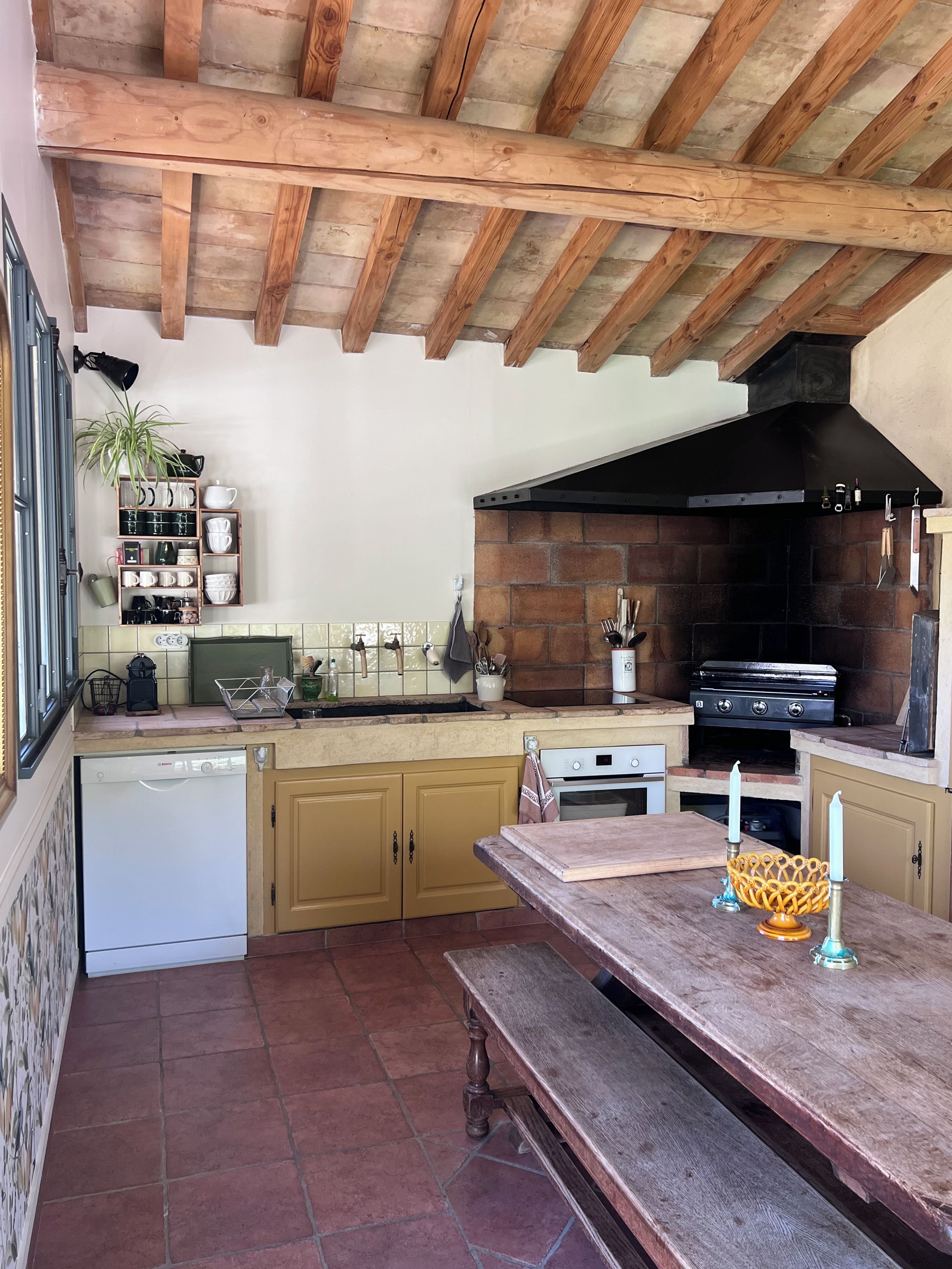 Une cuisine avec des poutres en bois, un mur en briques, un poêle noir et un banc en bois.