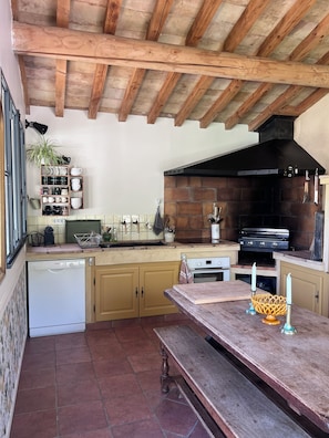 A kitchen with wooden beams, a brick wall, a black stove, and a wooden bench.