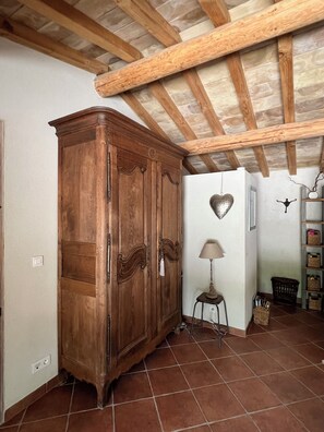 A room with a large wooden wardrobe, a small table with a lamp, and a tiled floor.