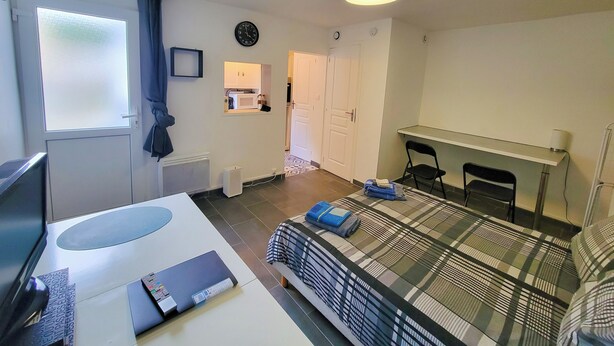 A bedroom with a bed, a desk, a chair, a TV, and a window with curtains.