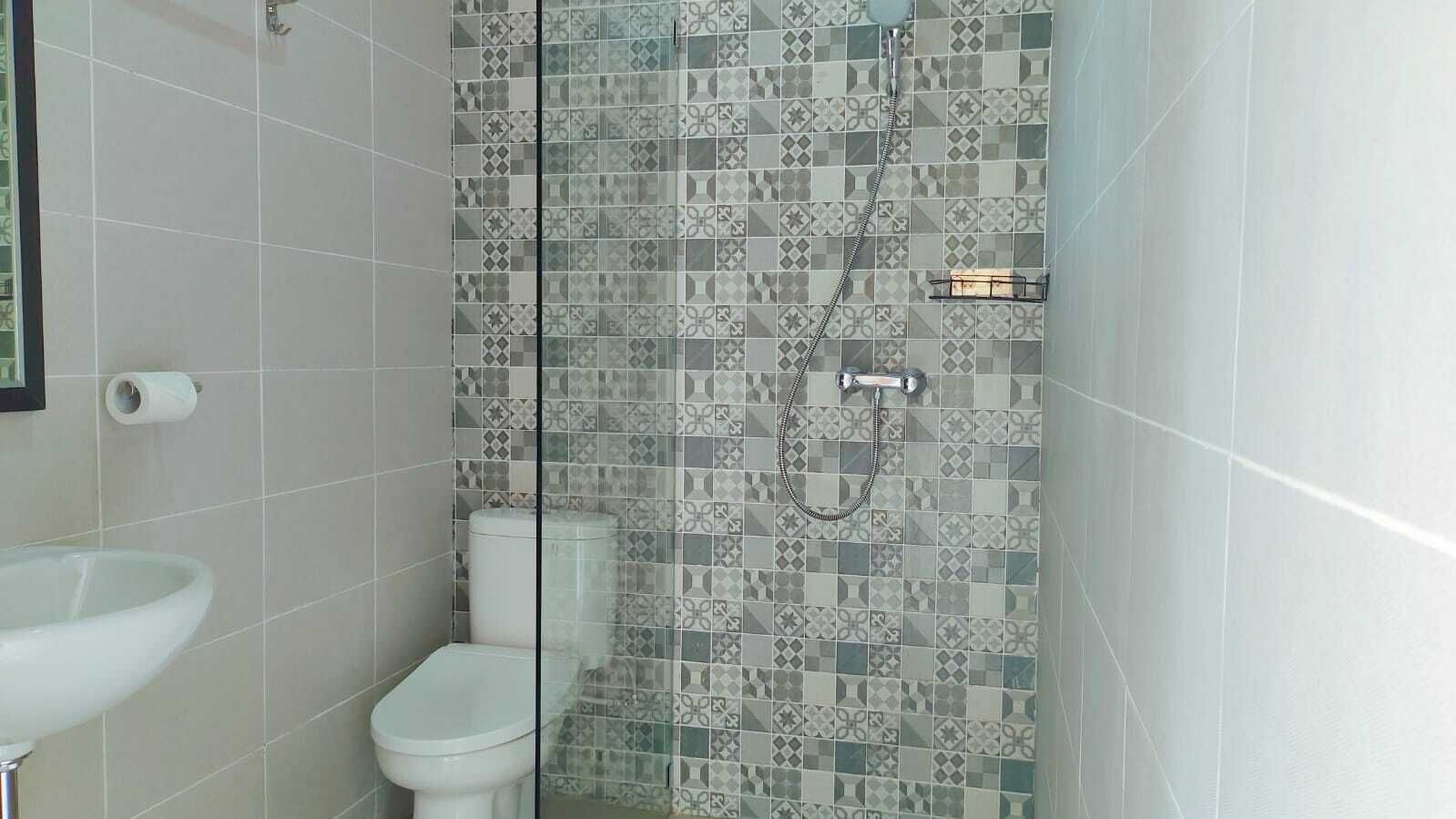 Une salle de bain équipée de toilettes, d’un lavabo et d’une douche dont les carreaux de revêtement présentent un motif.