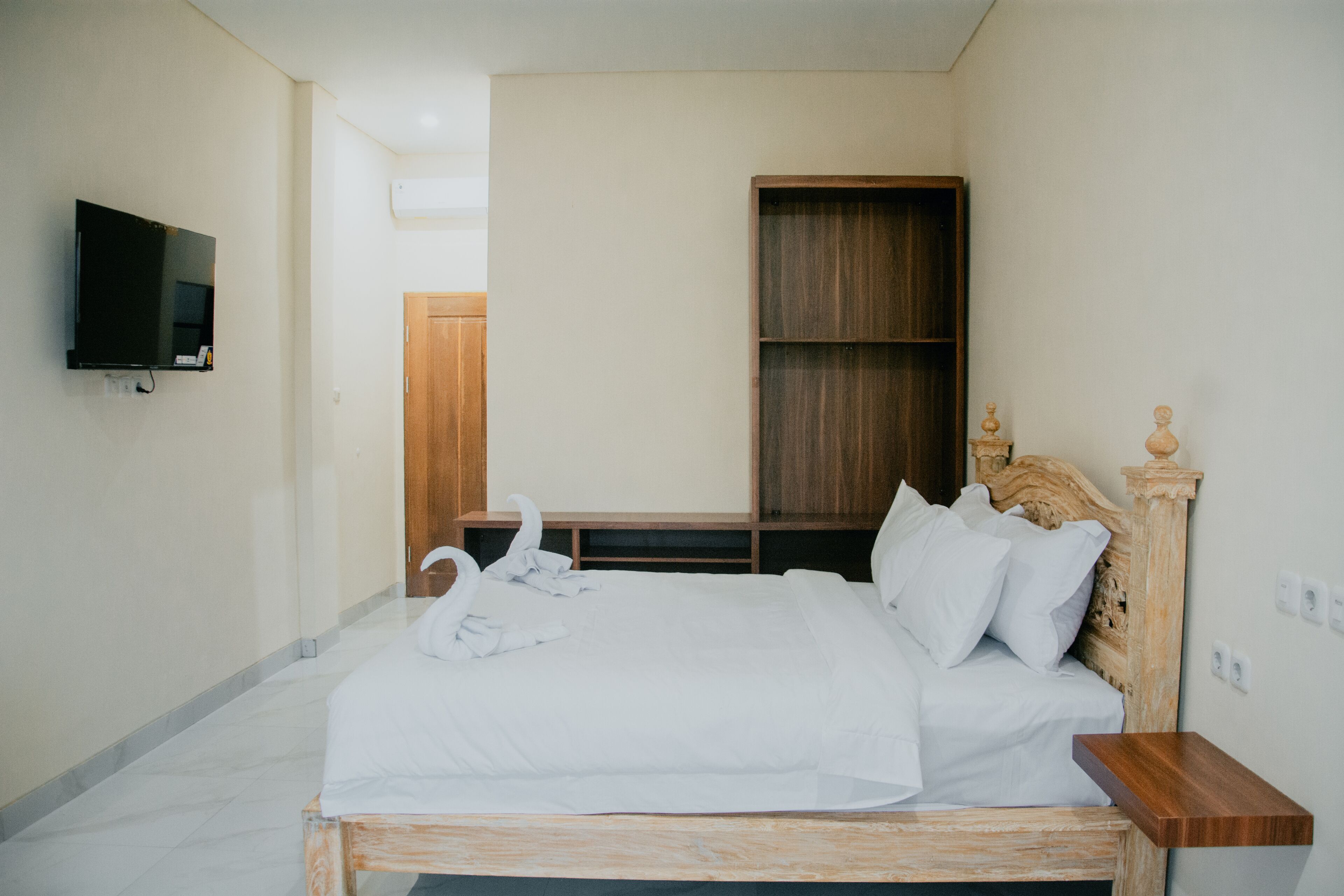A hotel room with a bed, a TV mounted on the wall, and a wooden wardrobe.