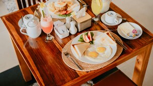 Tavolo di legno apparecchiato per la colazione, con uova, pane tostato e una bevanda, più teiera e condimento.
