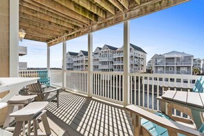 A wooden deck with outdoor seating, overlooking a marina with waterfront buildings.