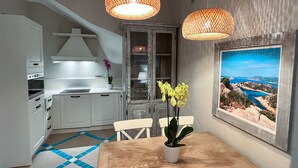 Una cocina moderna con armarios blancos, una mesa de comedor de madera y dos lámparas naranjas colgantes.