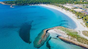 Luftaufnahme einer Küstenlandschaft mit klarem, blauem Meer, einem Sandstrand und einer felsigen Küstenlinie.