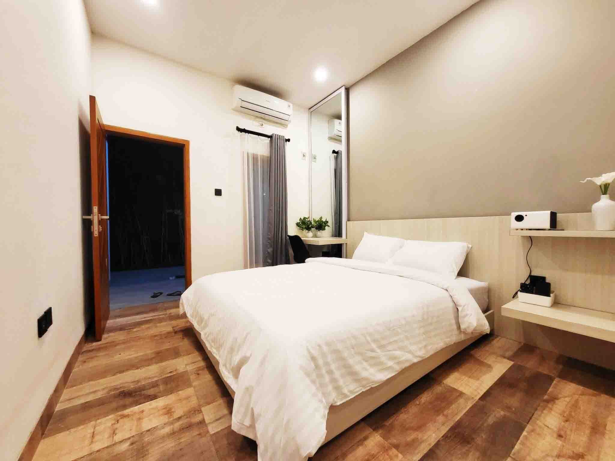 Un dormitorio moderno con una cama grande, suelo de madera, una mesita de noche con una planta, un espejo y un equipo de aire acondicionado.