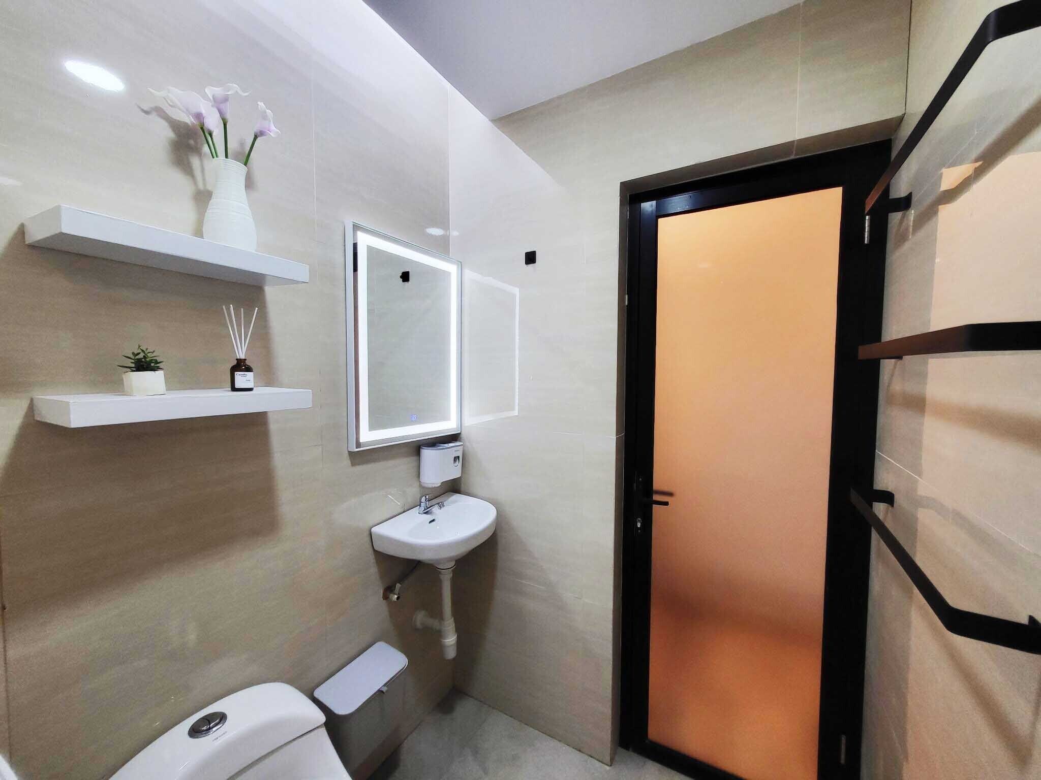 Ein kleines Badezimmer mit Toilette, Waschbecken und Spiegel. Regale mit einer Topfpflanze und einer Reed-Diffusor-Flasche.