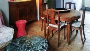 Et spiseområde med et træbord og stole, en rød stol, et bord af sort marmor, et træskab, en lampe og et billede i ramme på væggen.