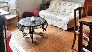 Et hyggeligt rum med trægulv, et rundt bord med en hvid genstand på, en seng med blomstret sengetæppe, et indrammet billede på væggen og en hængende lampe.
