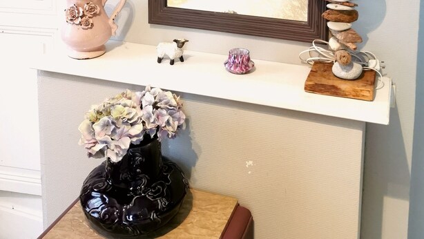 Et soveværelse med seng, kommode, spejl, lampe og en vase med blomster.