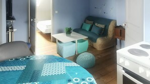 Een kamer met een bed, een slaapbank, een kleine tafel, een hanglamp en een fornuis.